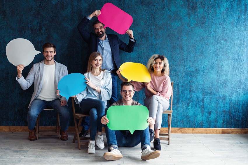 Five people sitting down smiling and holding cardboard cut outs of speech bubbles.